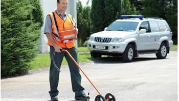 Ein Mann trägt eine orangefarbene Weste und fährt mit einem Gasspürgerät über die Straße